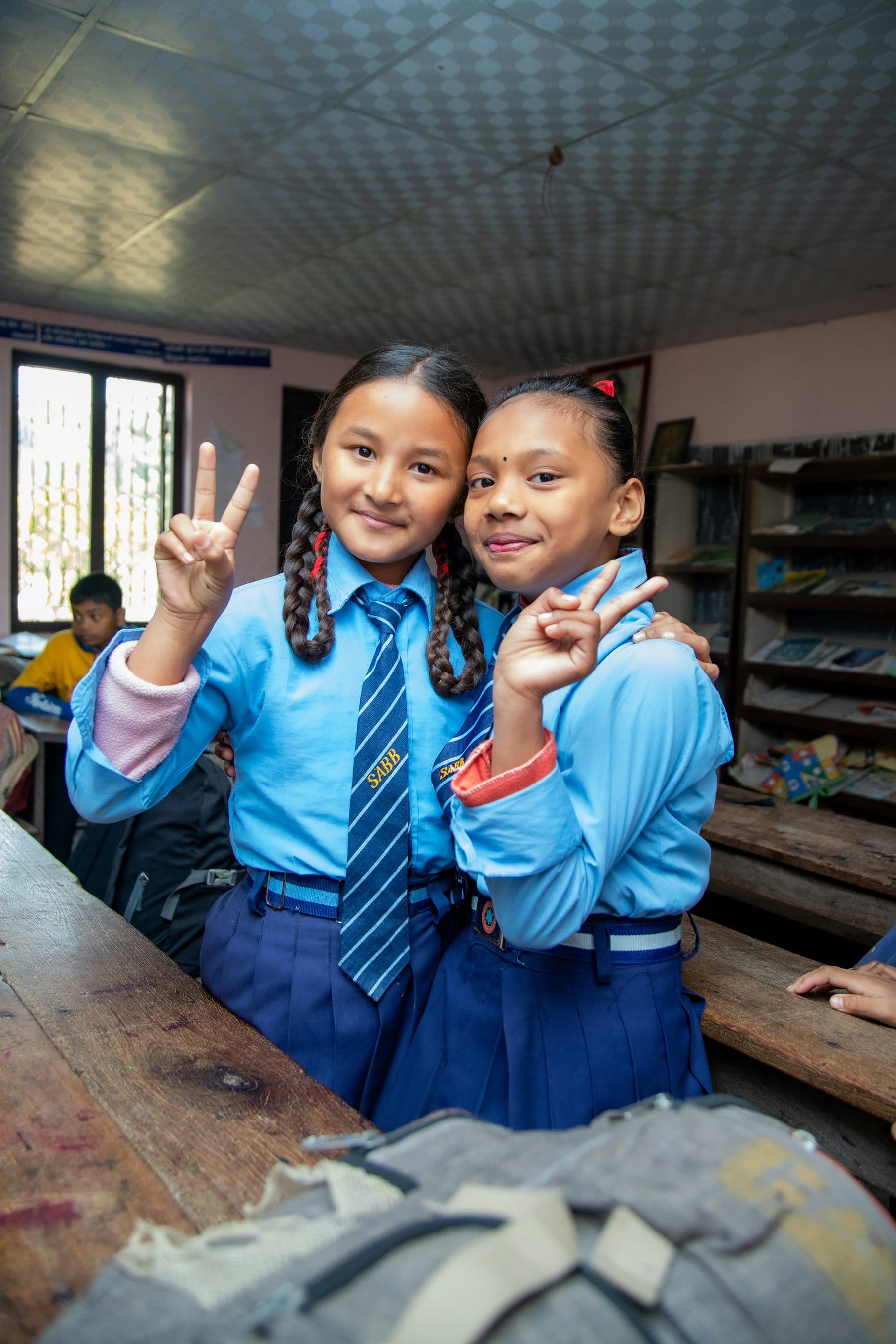 Two smiling Nepali schoolgirls sharing a light moment in class